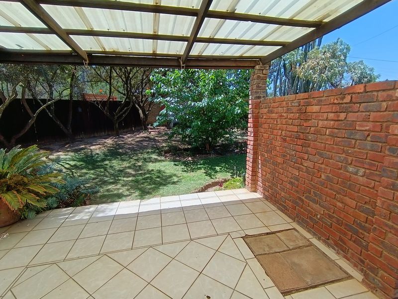 Covered outdoor patio featuring tiled flooring, an exposed brick wall, and a translucent roof structure overlooking a private garden area.