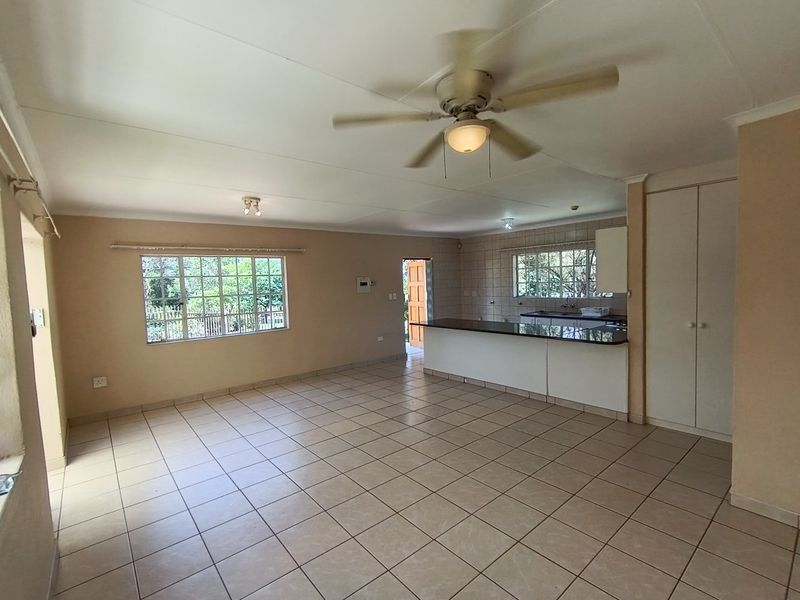 Spacious open-plan living area featuring tiled flooring, a ceiling fan, and a functional kitchen with granite countertops and ample built-in cabinetry.