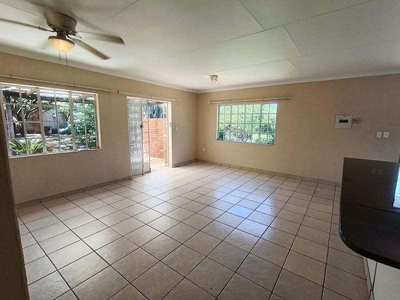 Spacious open-plan living area featuring neutral tiled flooring, ceiling fan, and direct access to the outdoor patio through a security gate.