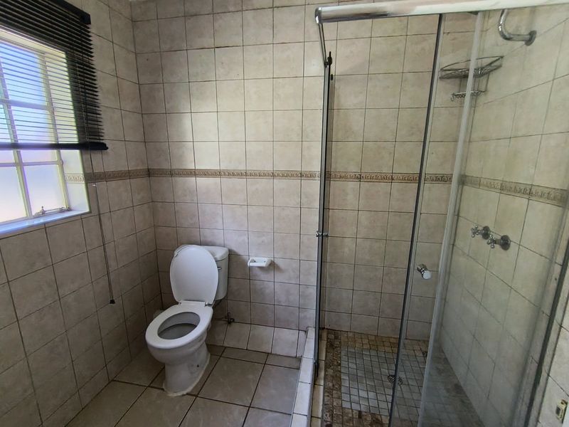 A functional bathroom featuring a shower enclosure, toilet, and neutral wall and floor tiling, requiring some cosmetic updates to improve its overall condition.