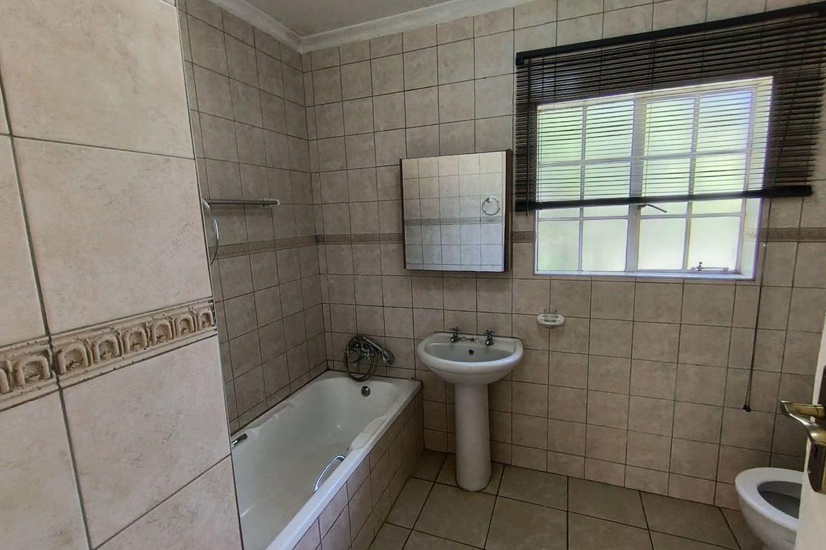 A functional bathroom featuring a pedestal basin, built-in bathtub, and full-height wall tiling, offering a neutral canvas for potential modern updates.