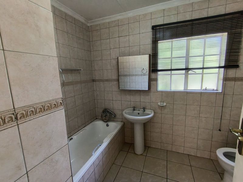 A functional bathroom featuring a pedestal basin, built-in bathtub, and full-height wall tiling, offering a neutral canvas for potential modern updates.
