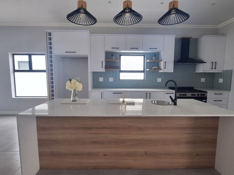 Modern kitchen featuring a central island with quartz countertops, sleek white cabinetry, integrated gas hob, extractor fan, and stylish pendant lighting.