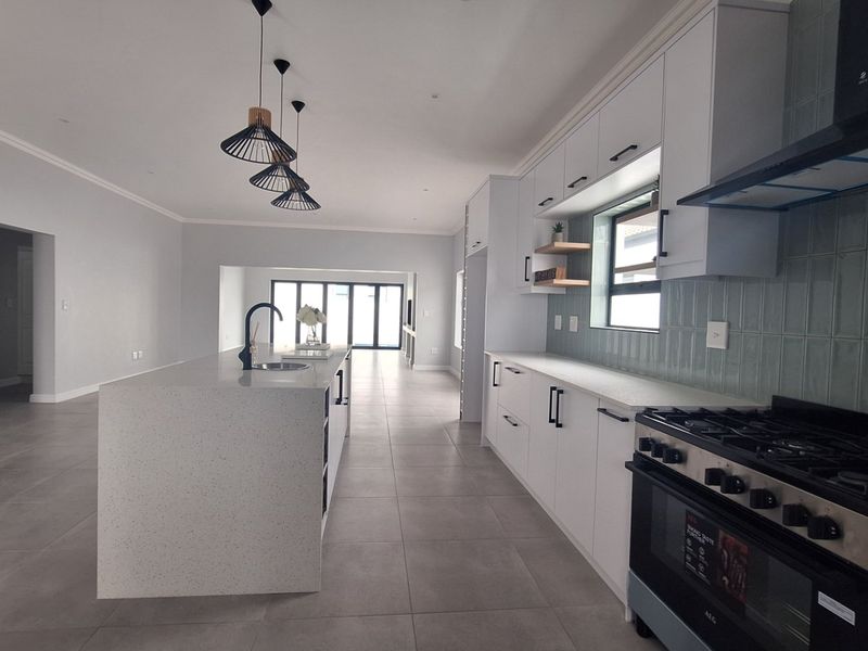 Modern open-plan kitchen featuring a large island with quartz countertops, gas stove, stylish pendant lighting, and contemporary cabinetry with a tiled backsplash.