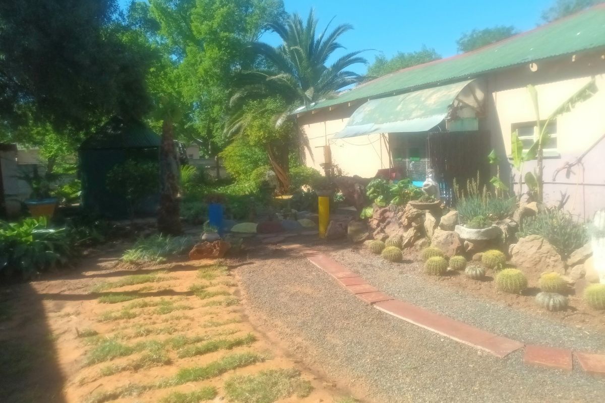 A rear garden area featuring a gravel pathway, rock landscaping, and a building with a corrugated metal roof and an attached awning.