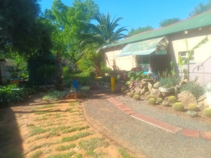 A rear garden area featuring a gravel pathway, rock landscaping, and a building with a corrugated metal roof and an attached awning.
