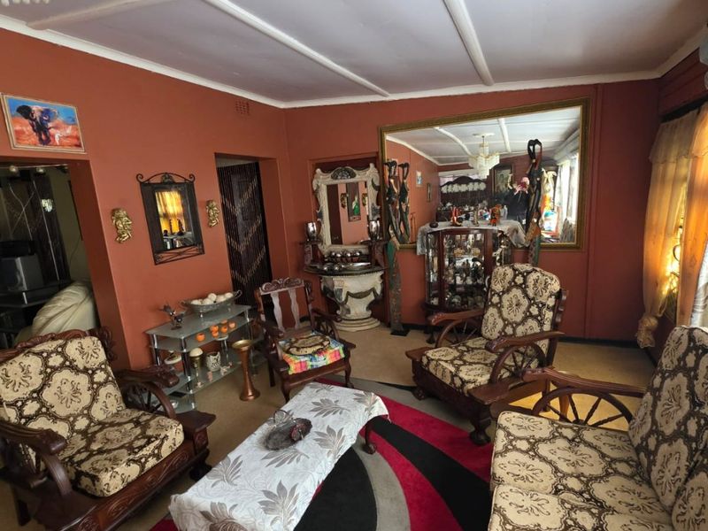A living room featuring an exposed beam ceiling and a large wall-mounted mirror, providing a traditional layout with potential for modern updates.