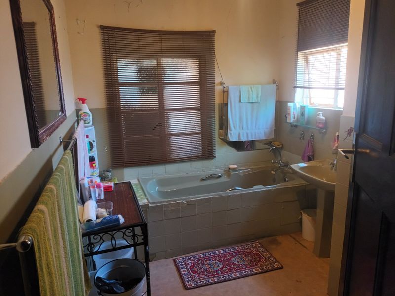A dated bathroom featuring a built-in bathtub with tiled surround and a pedestal sink, requiring cosmetic updates and ceiling repairs.