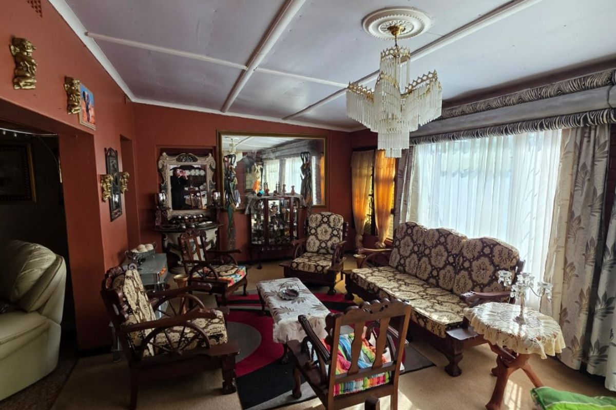 A spacious living room featuring a classic crystal chandelier, ceiling rose, and large window with a decorative pelmet, offering a traditional layout.