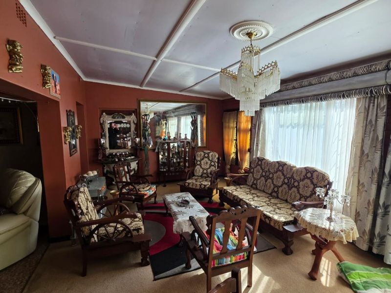 A spacious living room featuring a classic crystal chandelier, ceiling rose, and large window with a decorative pelmet, offering a traditional layout.