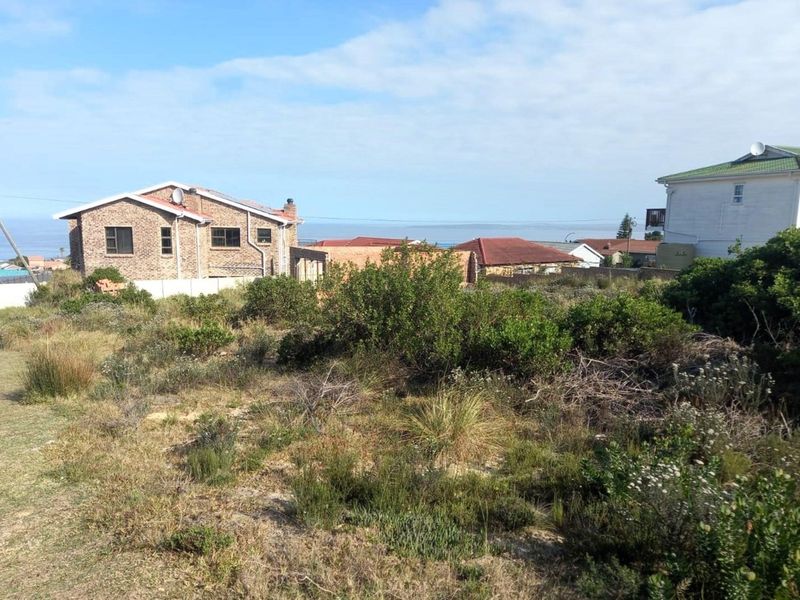 A view of a vacant residential plot featuring natural coastal vegetation with surrounding established homes in a quiet neighborhood setting.