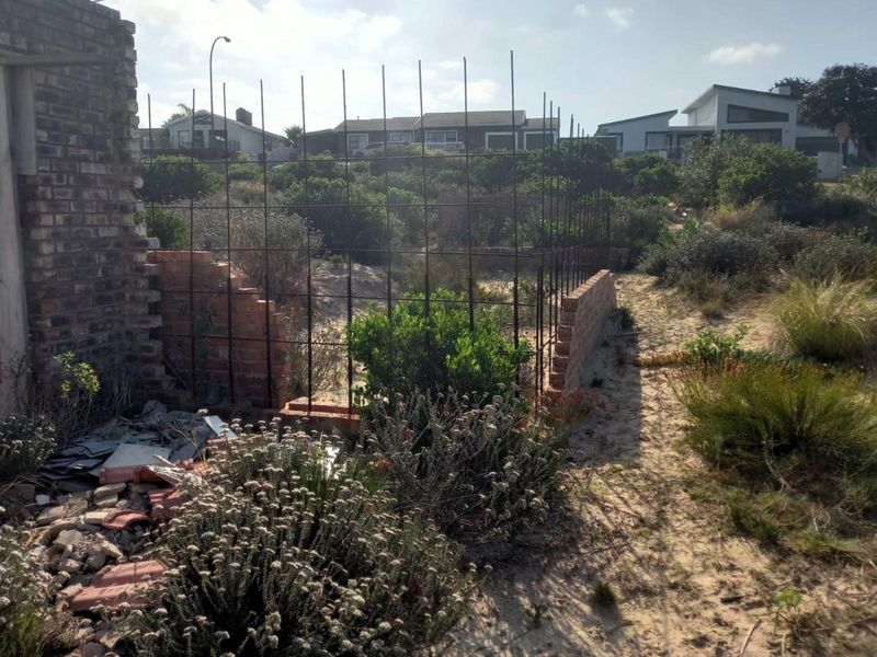 Vacant residential land featuring incomplete brick masonry walls and exposed steel reinforcement bars set within a natural coastal landscape.