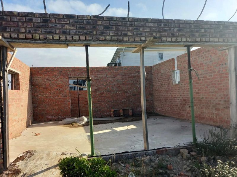An unfinished brick structure showing exposed masonry walls and a concrete slab foundation, currently supported by temporary steel props.
