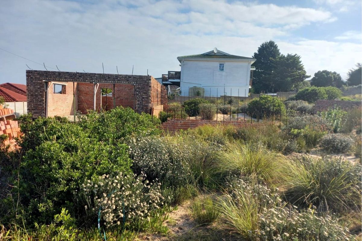 A residential plot featuring an incomplete brick structure, established garden vegetation, and existing boundary fencing in a suburban setting.