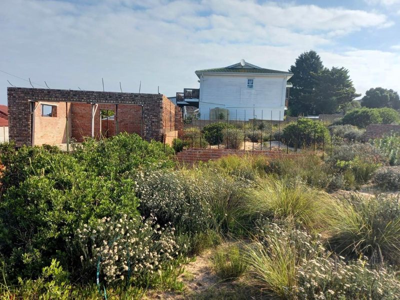 A residential plot featuring an incomplete brick structure, established garden vegetation, and existing boundary fencing in a suburban setting.