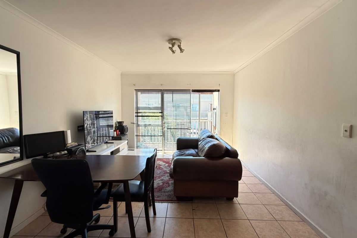 A living room featuring tiled flooring, cove cornicing, and a sliding glass door leading to an outdoor area. The walls show signs of wear.