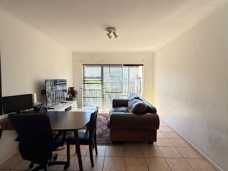 A living room featuring tiled flooring, cove cornicing, and a sliding glass door leading to an outdoor area. The walls show signs of wear.