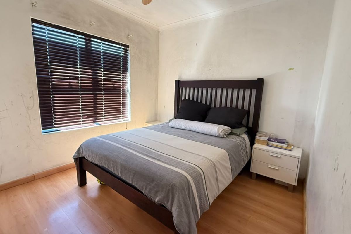 A bedroom featuring laminate flooring and venetian blinds, currently requiring wall repairs and repainting to restore the space.