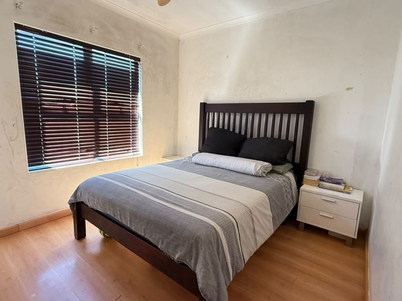 A bedroom featuring laminate flooring and venetian blinds, currently requiring wall repairs and repainting to restore the space.