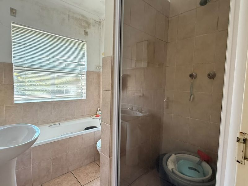 Bathroom featuring a pedestal basin, built-in bathtub, and separate shower enclosure with tiled finishes. Requires maintenance to address ceiling and wall surface damage.
