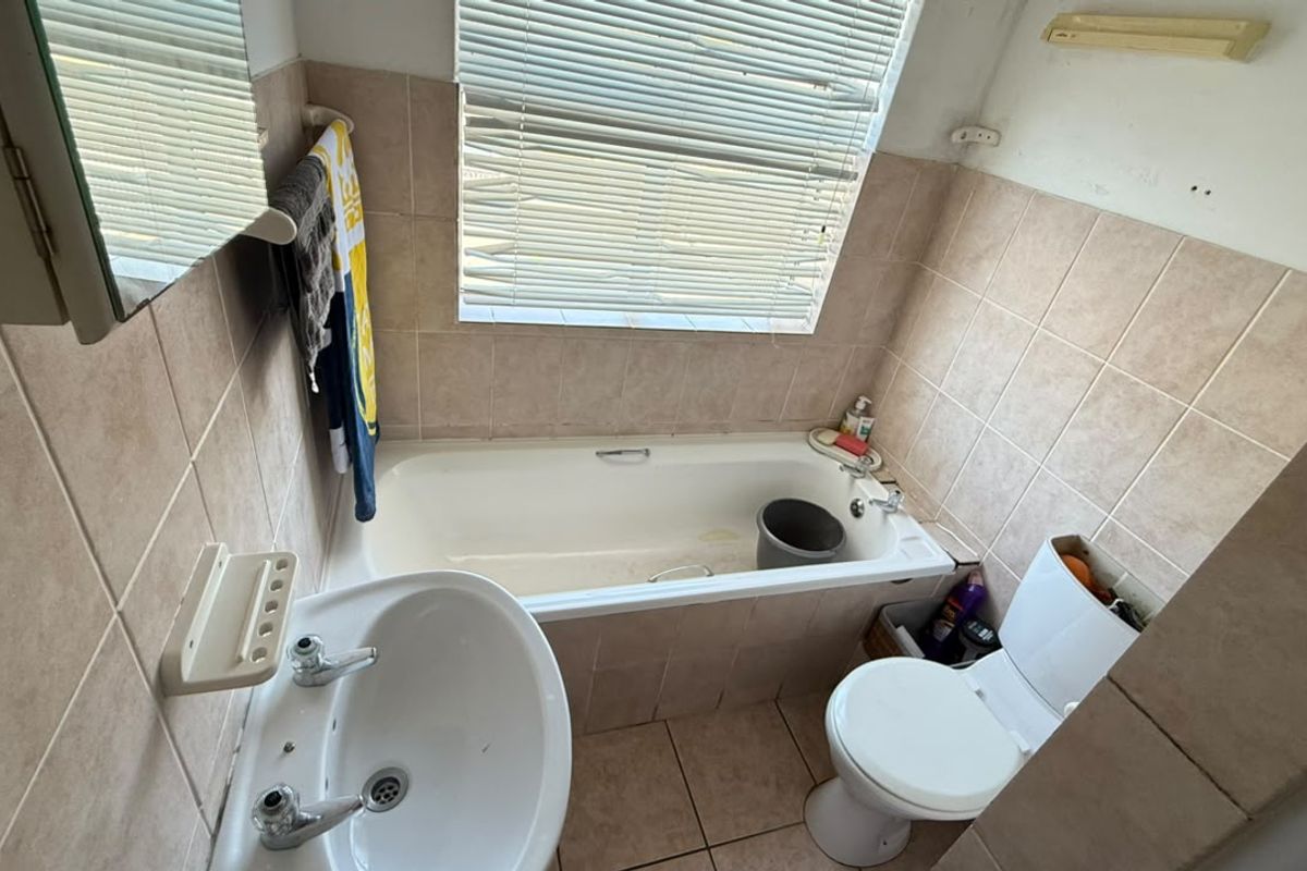 Compact bathroom featuring a bathtub, pedestal basin, and toilet with neutral wall and floor tiling, requiring some cosmetic updates.