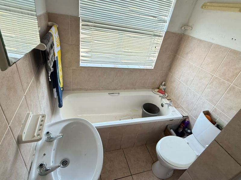 Compact bathroom featuring a bathtub, pedestal basin, and toilet with neutral wall and floor tiling, requiring some cosmetic updates.