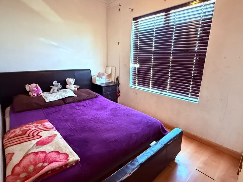 A bedroom featuring laminate flooring and venetian blinds, currently requiring cosmetic updates to the wall finishes.