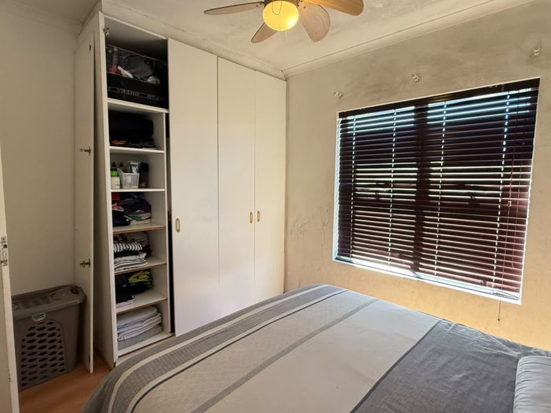 Bedroom featuring built-in cupboards, a ceiling fan, and venetian blinds. The walls require cosmetic attention and repainting.