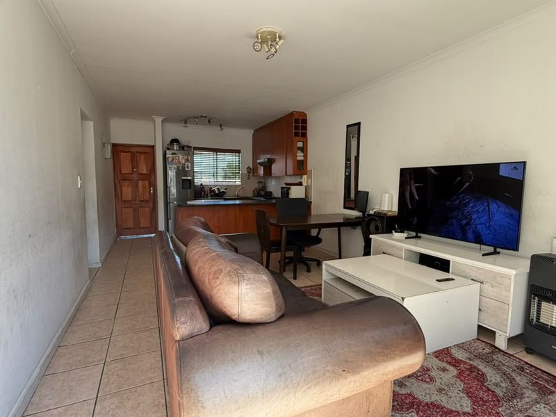 Open plan living and kitchen area featuring tiled flooring and wooden cabinetry, requiring cosmetic updates to the wall finishes.