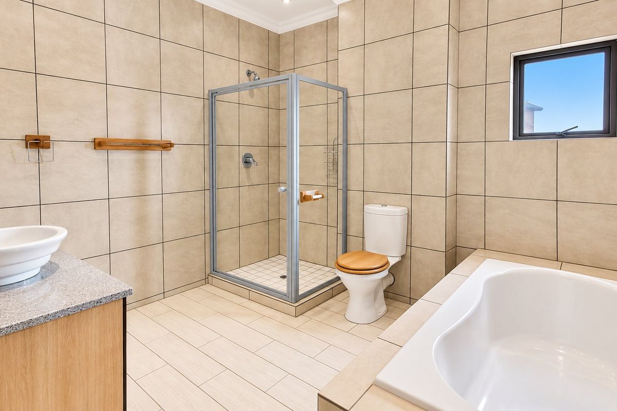 A modern, well-maintained bathroom featuring a glass shower enclosure, a built-in bathtub, a vanity with a vessel sink, and neutral floor-to-ceiling wall tiles.