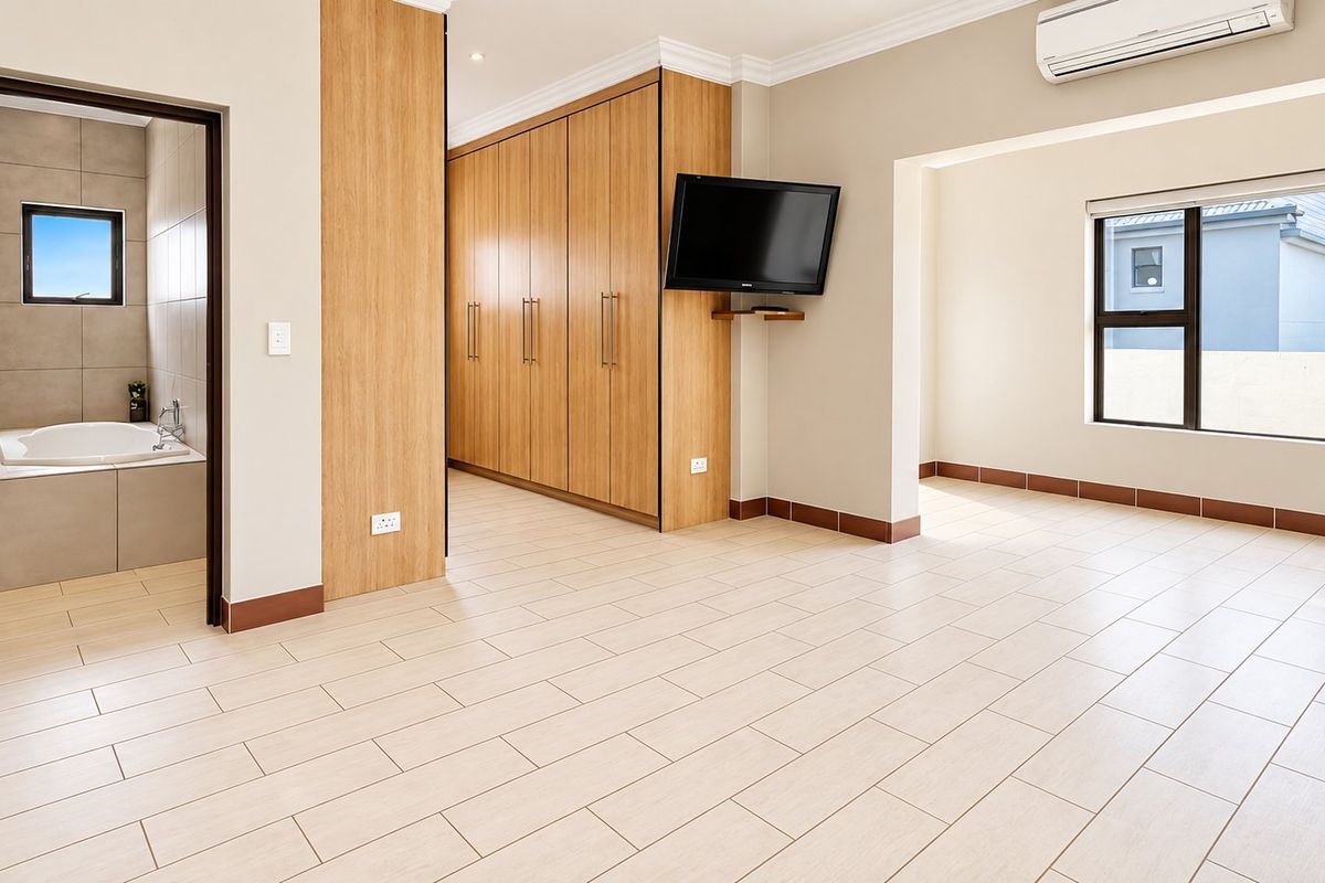 Spacious bedroom featuring light tiled flooring, extensive built-in cabinetry, an integrated air conditioning unit, and an adjoining en-suite bathroom with a built-in bathtub.