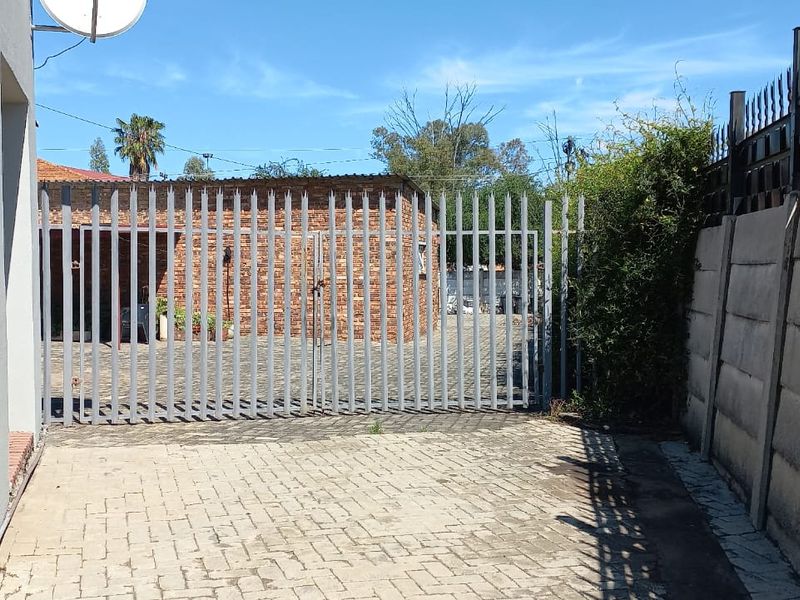 Front exterior view featuring a paved driveway, secure steel gate, and precast concrete boundary wall.
