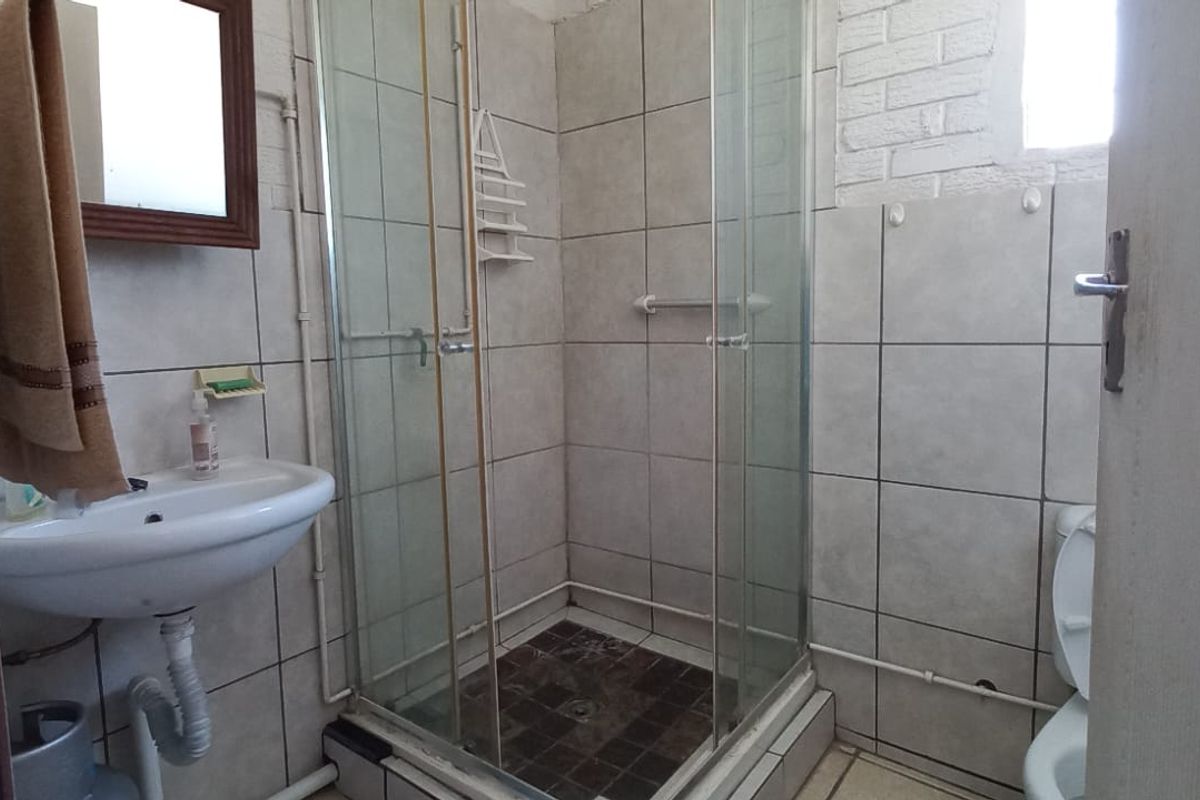 A functional bathroom featuring a shower enclosure, pedestal basin, and toilet with tiled finishes, requiring cosmetic updates to modernize the space.