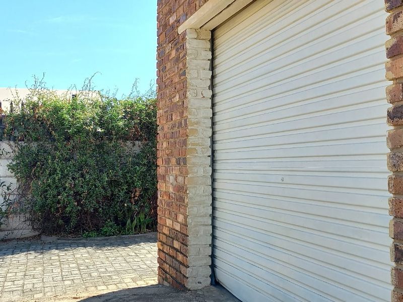 Exterior view of a face brick garage featuring a roller shutter door, adjacent to a paved driveway and a precast concrete boundary wall.