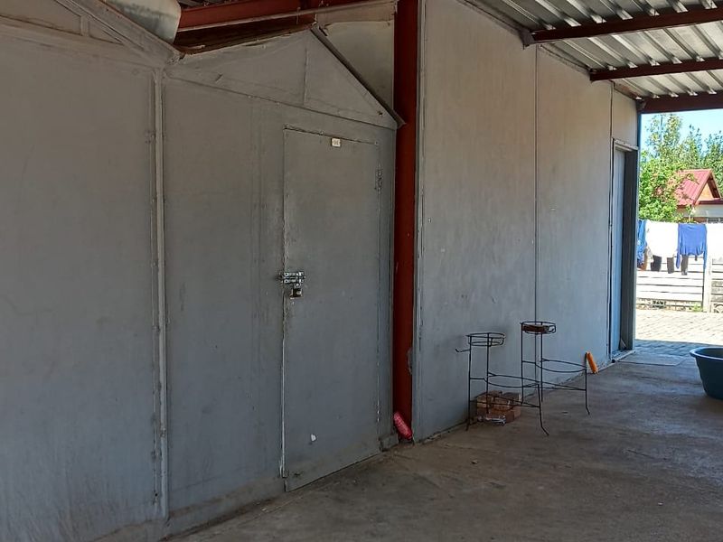 A functional, open-sided garage or utility area featuring metal wall panels, a corrugated roof structure, and concrete flooring.