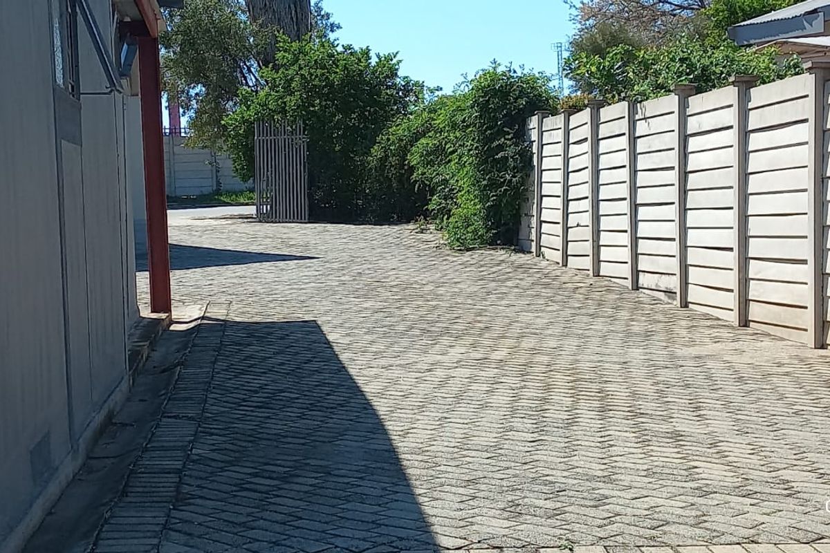 A paved side driveway area featuring a precast concrete boundary wall and metal gate access.