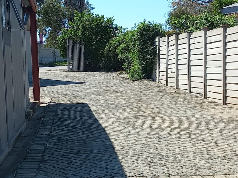 A paved side driveway area featuring a precast concrete boundary wall and metal gate access.