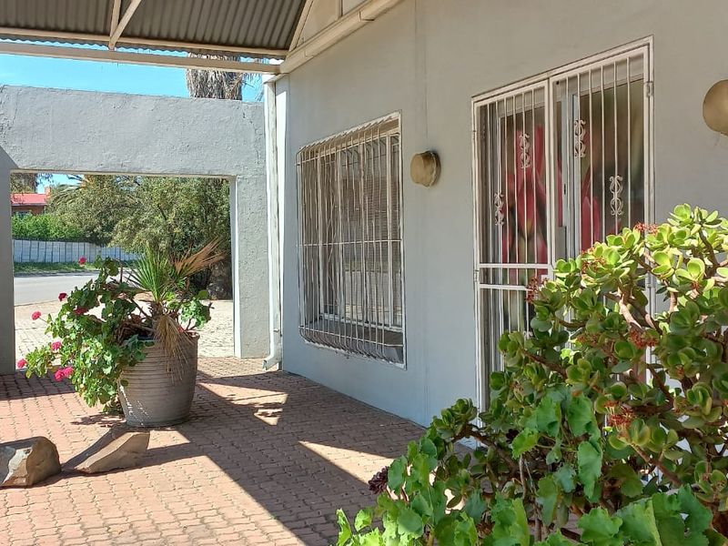 A covered outdoor patio area featuring paved flooring, security gates, and protective window bars, providing a functional transition space between the home and garden.