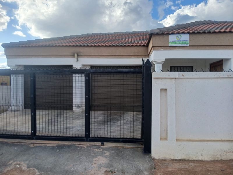 Front elevation of the property featuring a tiled roof, secure perimeter wall with spikes, and a gated driveway entrance.