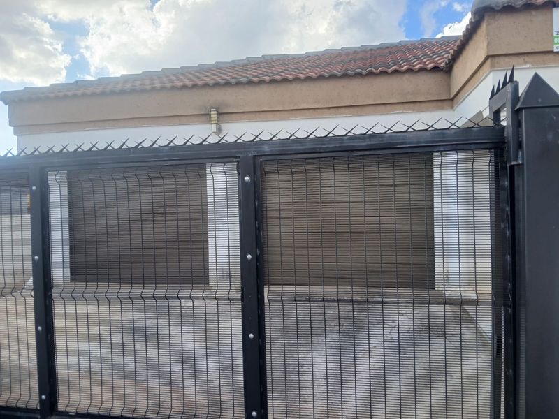 Front exterior view featuring a secure metal gate, spiked fencing, and roller shutter doors covering the garage entrance.
