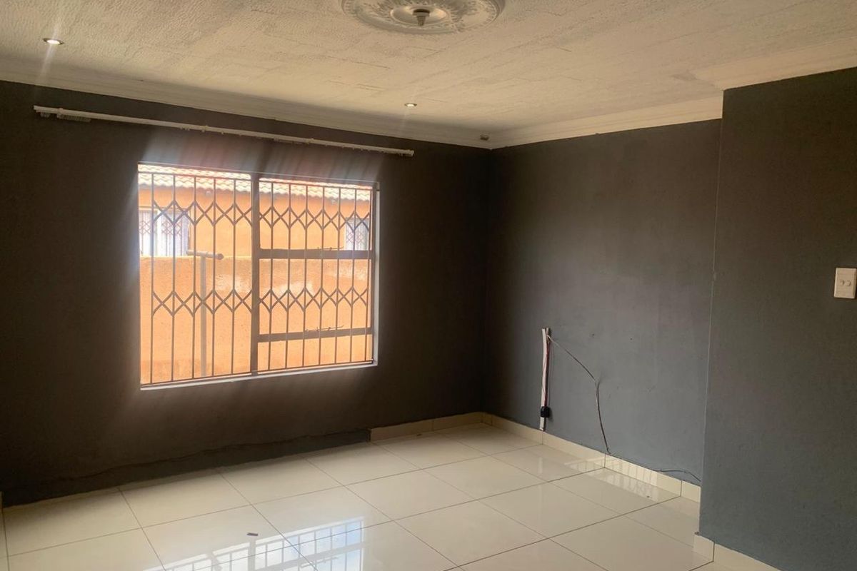 An empty living room featuring tiled flooring, a decorative ceiling rose, recessed lighting, and a window fitted with a security gate.