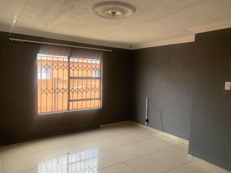 An empty living room featuring tiled flooring, a decorative ceiling rose, recessed lighting, and a window fitted with a security gate.