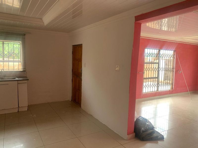 An open-plan living and kitchen area featuring tiled floors, security bars on windows, and a basic kitchen sink unit with cabinetry.