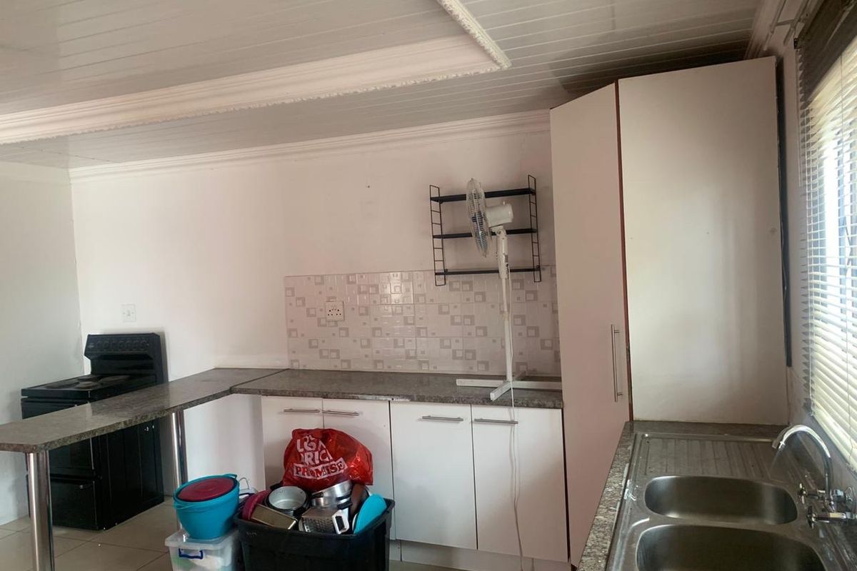 Functional kitchen featuring white cabinetry, laminate countertops, a double stainless steel sink, and a tiled splashback with a tongue and groove ceiling.