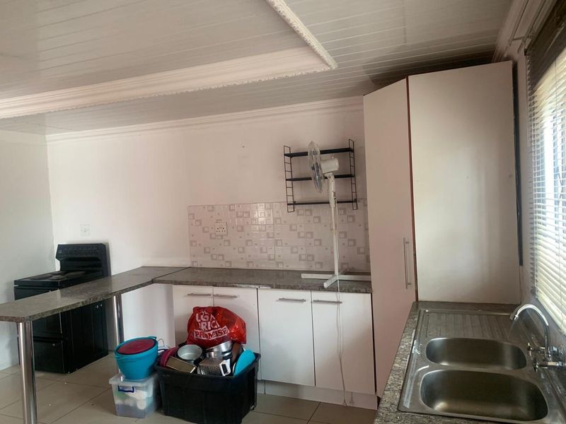 Functional kitchen featuring white cabinetry, laminate countertops, a double stainless steel sink, and a tiled splashback with a tongue and groove ceiling.
