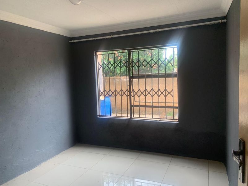 An empty bedroom featuring dark grey painted walls, white tiled flooring, and a window fitted with a metal security gate.