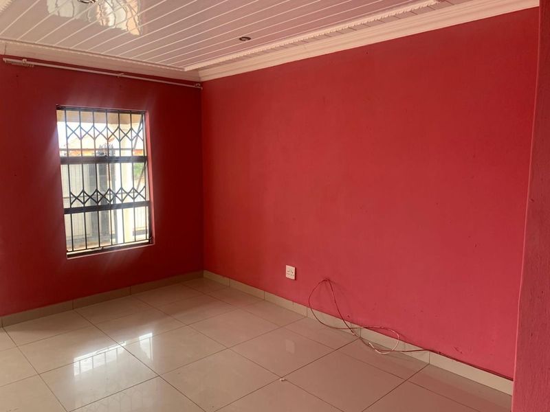 An empty bedroom featuring red painted walls, tiled flooring, a PVC ceiling, and a window fitted with security bars.