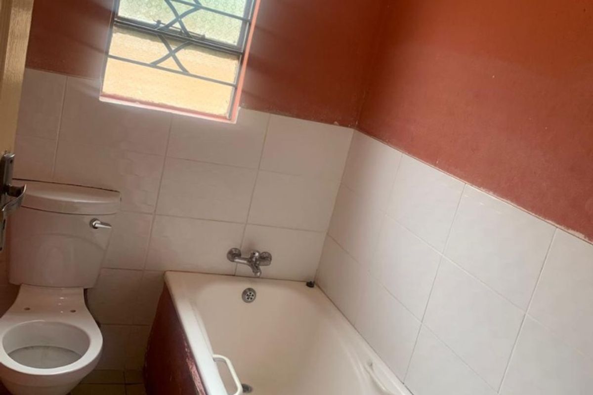 A functional bathroom featuring a standard bathtub, toilet, and tiled wall finishes, currently requiring cosmetic updates and paintwork.