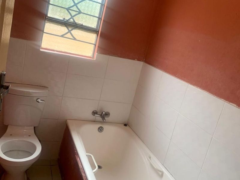 A functional bathroom featuring a standard bathtub, toilet, and tiled wall finishes, currently requiring cosmetic updates and paintwork.