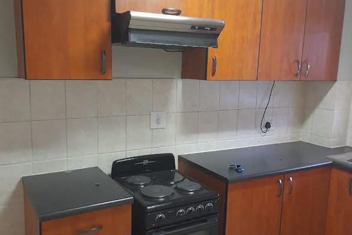 A functional kitchen featuring wood-look laminate cabinetry, dark countertops, a built-in electric stove with extractor fan, and neutral tiled backsplash and flooring.